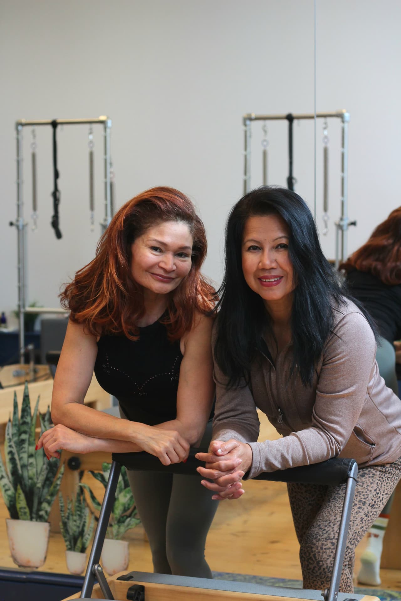 Rebecca and Adriana smiling as they lean on a Reformer footbar